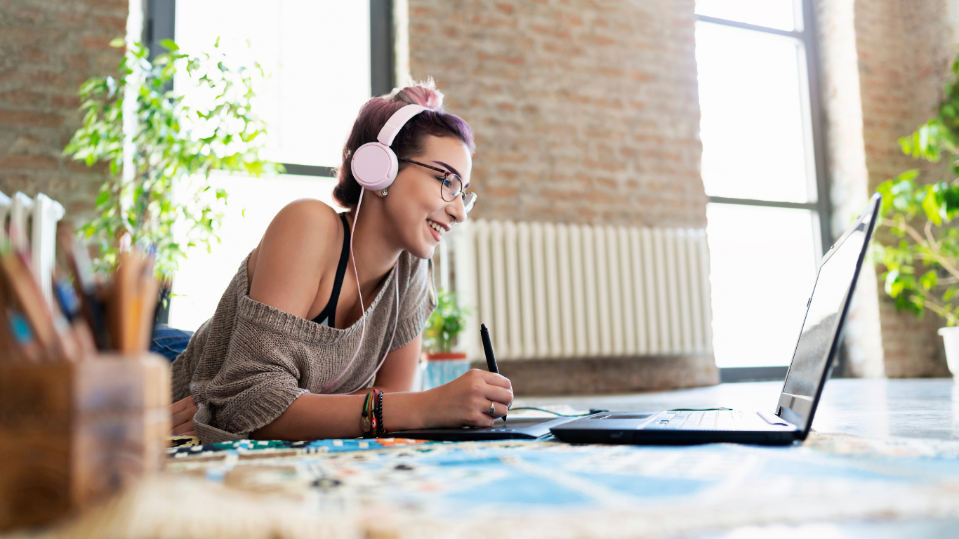 A student interacting on a computer while smiling and writing something in a notebook.
